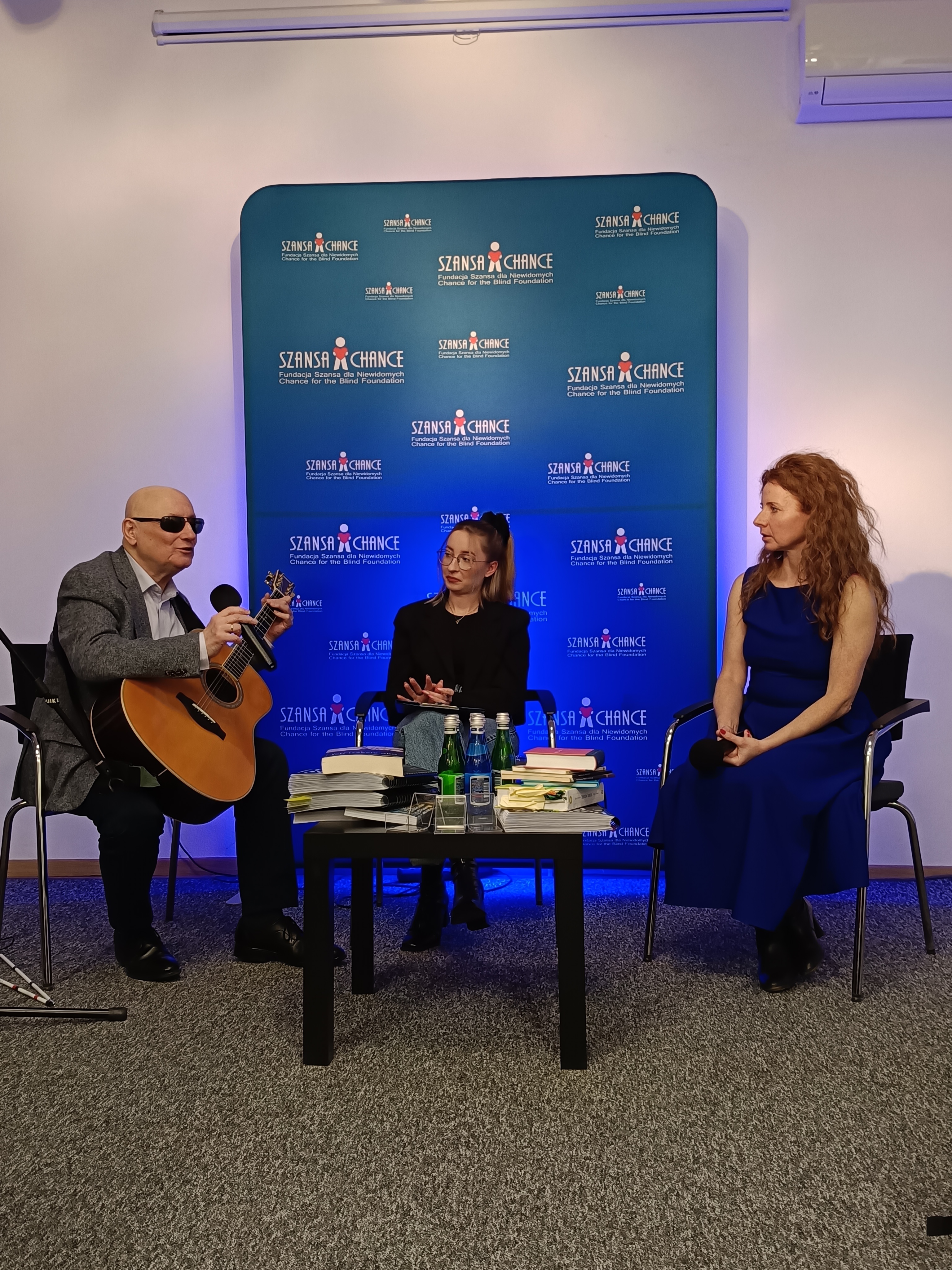 prezes Fundacji Marek Kalbarczyk z gitarą, redaktor Beata Jewiarz i pomysłodawczyni projektu "Pod rękę z poezją" Ewelina Mirocha podczas promocji książki